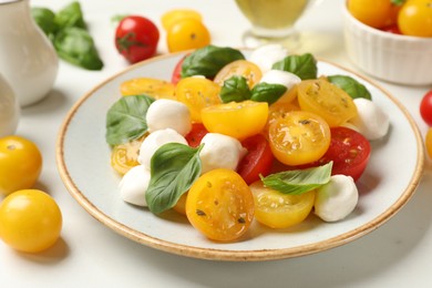 Photo of Fresh salad with yellow tomatoes, basil and mozzarella cheese on white table, closeup