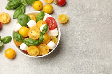 Photo of Fresh salad with yellow tomatoes, basil and mozzarella cheese on grey table, flat lay. Space for text