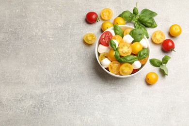 Photo of Fresh salad with yellow tomatoes, basil and mozzarella cheese on grey table, flat lay. Space for text