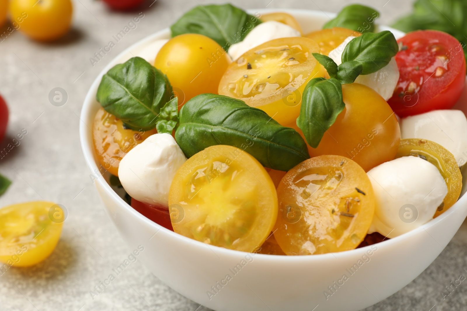 Fresh salad with yellow tomatoes, basil and mozzarella cheese on grey table, closeup Photo of Fresh salad with yellow tomatoes, basil and mozzarella cheese on grey table, closeup