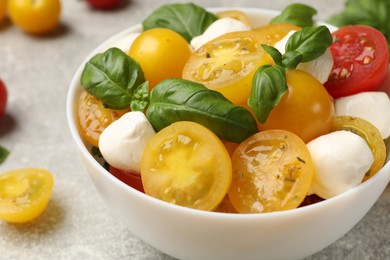 Photo of Fresh salad with yellow tomatoes, basil and mozzarella cheese on grey table, closeup
