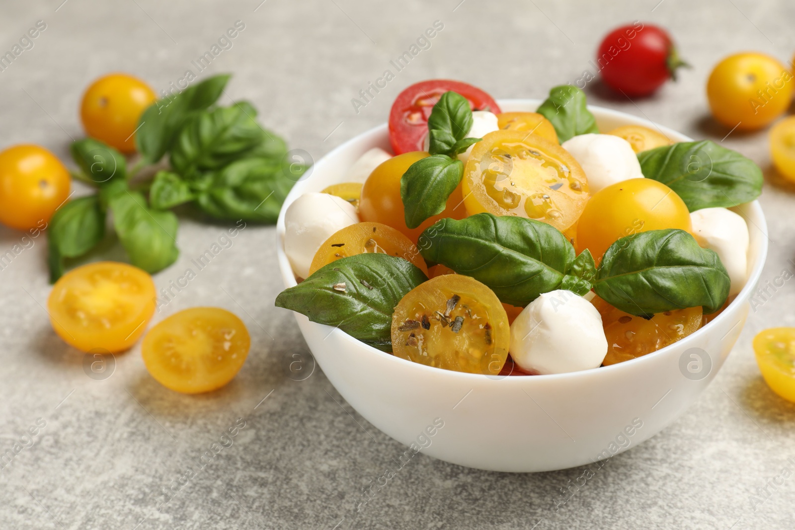 Fresh salad with yellow tomatoes, basil and mozzarella cheese on grey table, closeup Photo of Fresh salad with yellow tomatoes, basil and mozzarella cheese on grey table, closeup