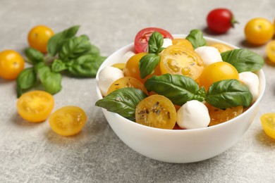 Photo of Fresh salad with yellow tomatoes, basil and mozzarella cheese on grey table, closeup