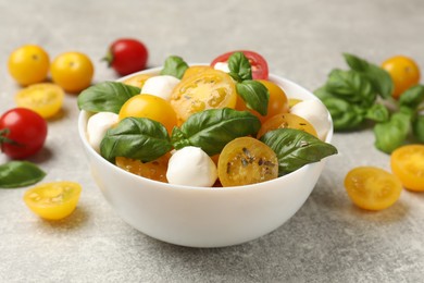 Photo of Fresh salad with yellow tomatoes, basil and mozzarella cheese on grey table, closeup