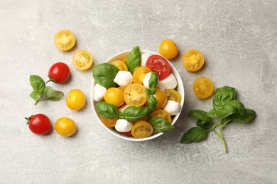 Photo of Fresh salad with yellow tomatoes, basil and mozzarella cheese on grey table, flat lay