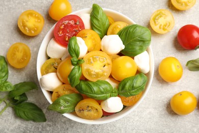 Photo of Fresh salad with yellow tomatoes, basil and mozzarella cheese on grey table, flat lay