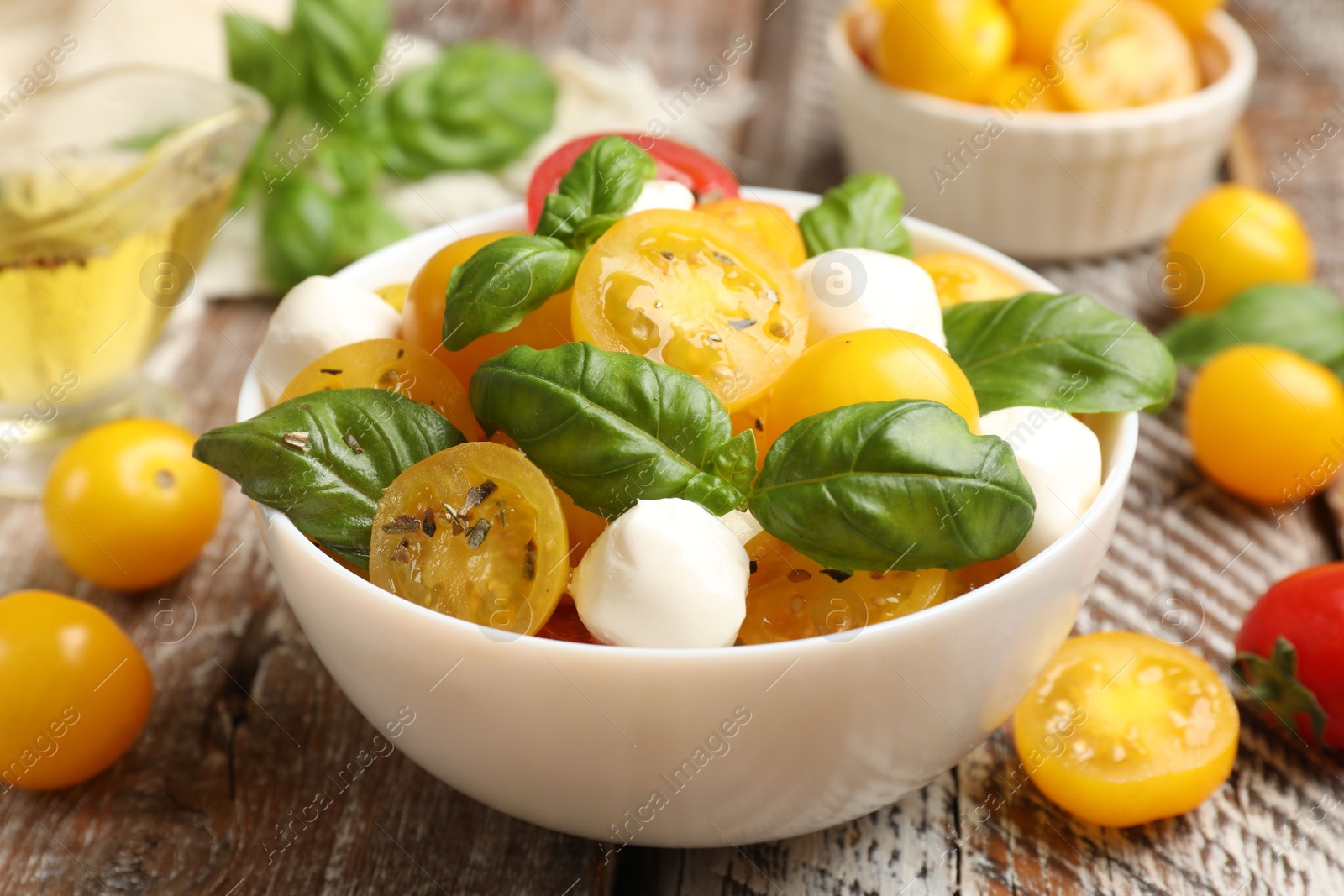 Fresh salad with yellow tomatoes, basil and mozzarella cheese on wooden table, closeup Photo of Fresh salad with yellow tomatoes, basil and mozzarella cheese on wooden table, closeup