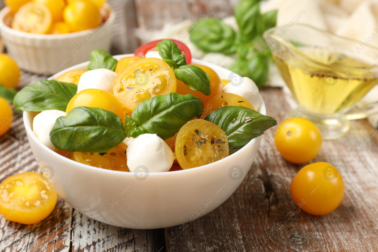 Fresh salad with yellow tomatoes, basil and mozzarella cheese on wooden table, closeup Photo of Fresh salad with yellow tomatoes, basil and mozzarella cheese on wooden table, closeup