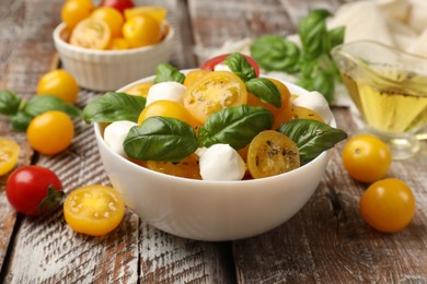 Photo of Fresh salad with yellow tomatoes, basil and mozzarella cheese on wooden table, closeup