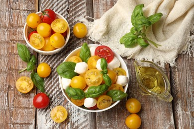 Photo of Fresh salad with yellow tomatoes, basil and mozzarella cheese on wooden table, flat lay