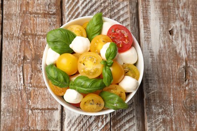 Photo of Fresh salad with yellow tomatoes, basil and mozzarella cheese in bowl on wooden table, top view