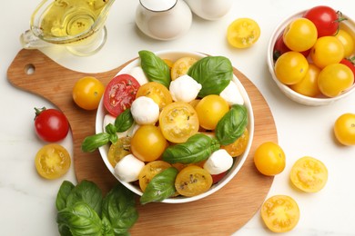 Photo of Fresh salad with yellow tomatoes, basil and mozzarella cheese on white marble table, flat lay
