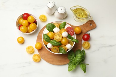 Photo of Fresh salad with yellow tomatoes, basil and mozzarella cheese on white marble table, flat lay