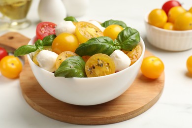 Photo of Fresh salad with yellow tomatoes, basil and mozzarella cheese on white table, closeup