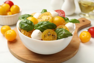 Photo of Fresh salad with yellow tomatoes, basil and mozzarella cheese on white table, closeup
