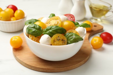 Photo of Fresh salad with yellow tomatoes, basil and mozzarella cheese on white table, closeup