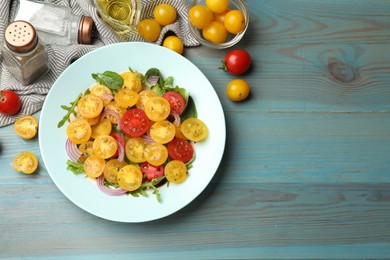Photo of Fresh salad with yellow tomatoes served on light blue wooden table, flat lay. Space for text