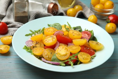 Photo of Fresh salad with yellow tomatoes served on light blue wooden table, closeup