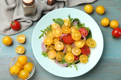 Photo of Fresh salad with yellow tomatoes served on light blue wooden table, flat lay