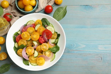 Photo of Fresh salad with yellow tomatoes served on light blue wooden table, flat lay. Space for text
