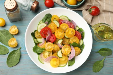 Photo of Fresh salad with yellow tomatoes served on light blue wooden table, flat lay