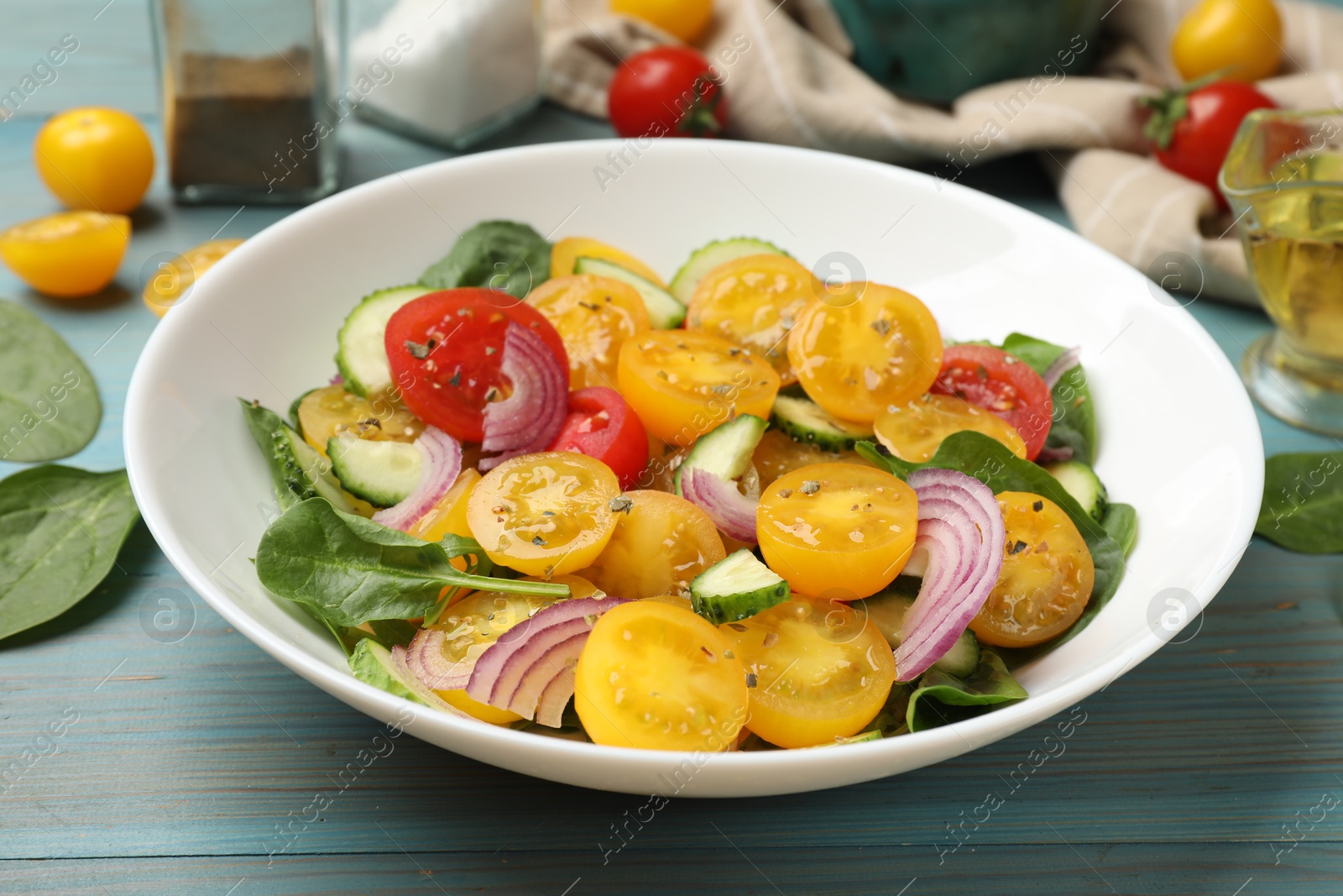 Fresh salad with yellow tomatoes served on light blue wooden table, closeup Photo of Fresh salad with yellow tomatoes served on light blue wooden table, closeup