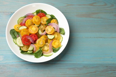 Photo of Fresh salad with yellow tomatoes on light blue wooden table, top view. Space for text