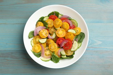 Photo of Fresh salad with yellow tomatoes on light blue wooden table, top view