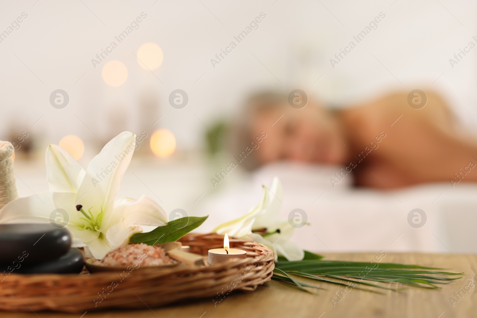 Senior woman relaxing on massage couch indoors, selective focus. Different spa products and lily flowers on table Photo of Senior woman relaxing on massage couch indoors, selective focus. Different spa products and lily flowers on table