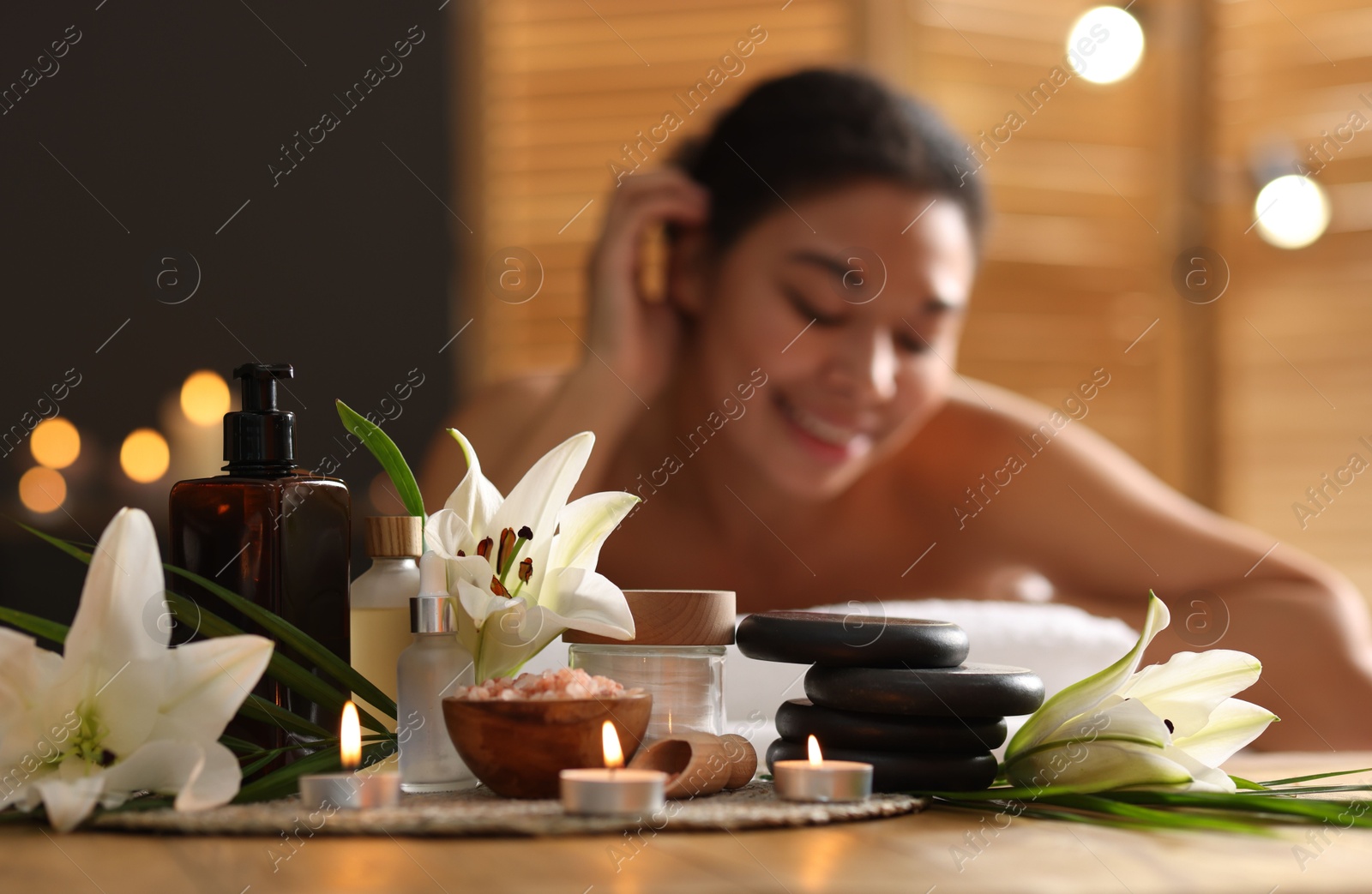 Beautiful woman relaxing on massage couch indoors, focus on different spa products and lily flowers Photo of Beautiful woman relaxing on massage couch indoors, focus on different spa products and lily flowers