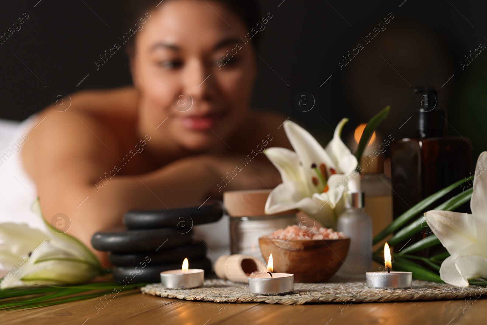 Beautiful woman relaxing on massage couch indoors, focus on different spa products and lily flowers Photo of Beautiful woman relaxing on massage couch indoors, focus on different spa products and lily flowers