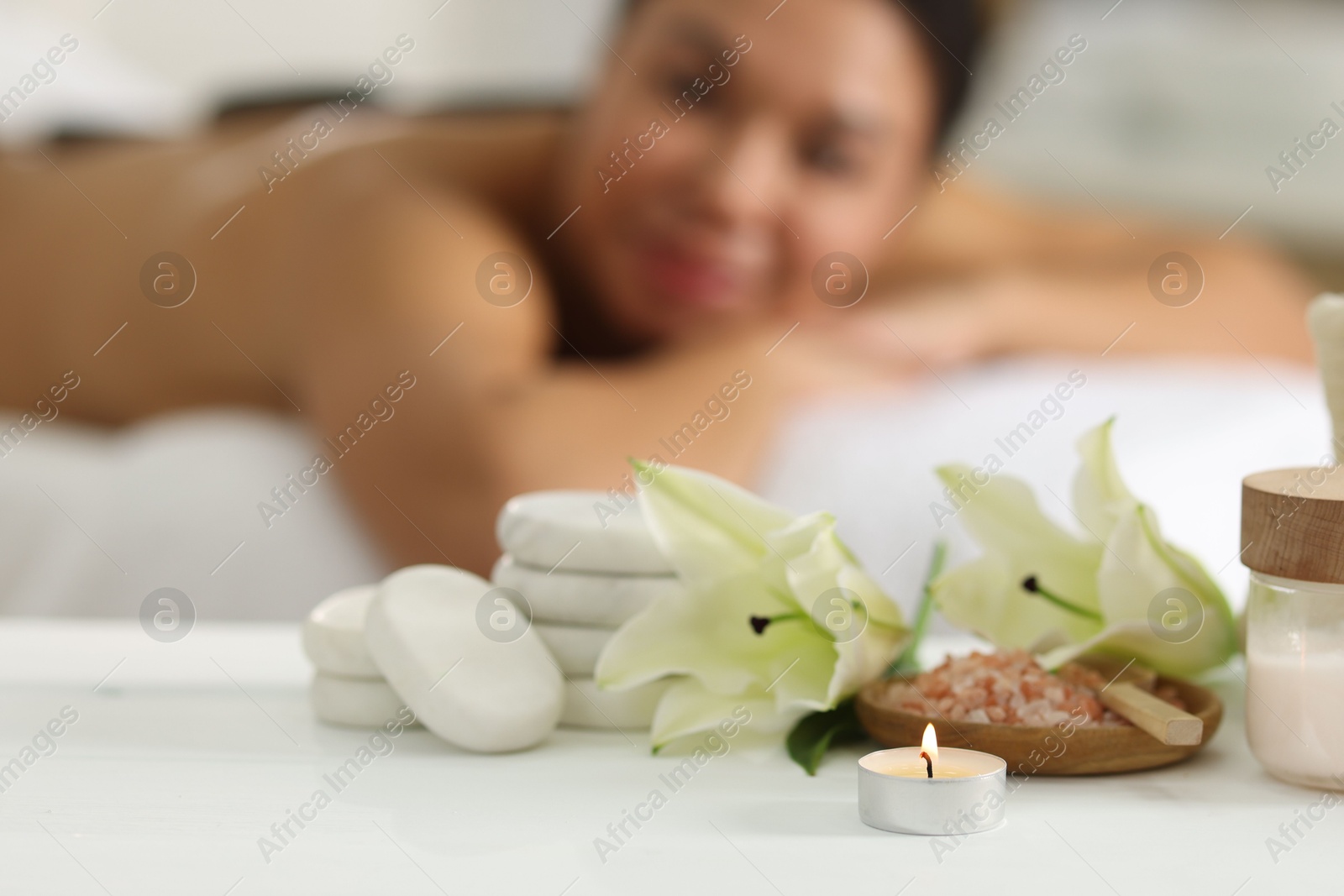 Photo of Beautiful woman relaxing on massage couch indoors, focus on different spa products and lily flowers