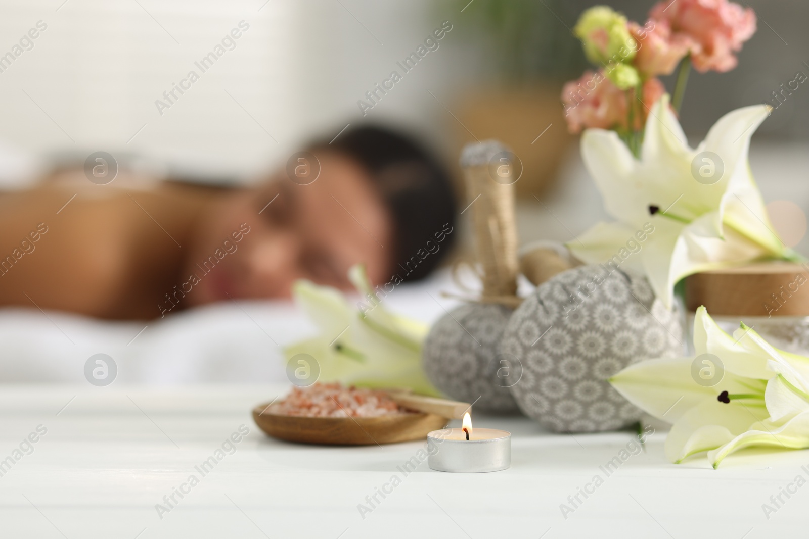 Beautiful woman relaxing on massage couch indoors, focus on different spa products and lily flowers Photo of Beautiful woman relaxing on massage couch indoors, focus on different spa products and lily flowers