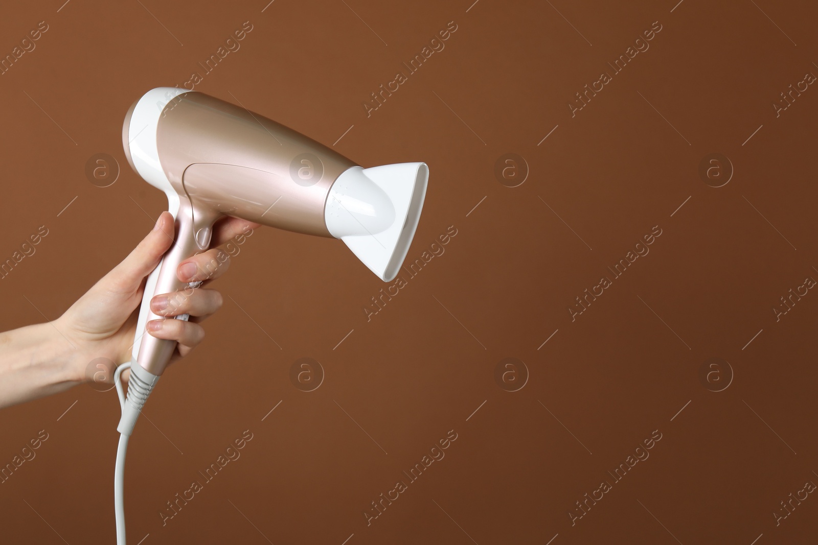 Photo of Woman with hair dryer on brown background, closeup. Space for text