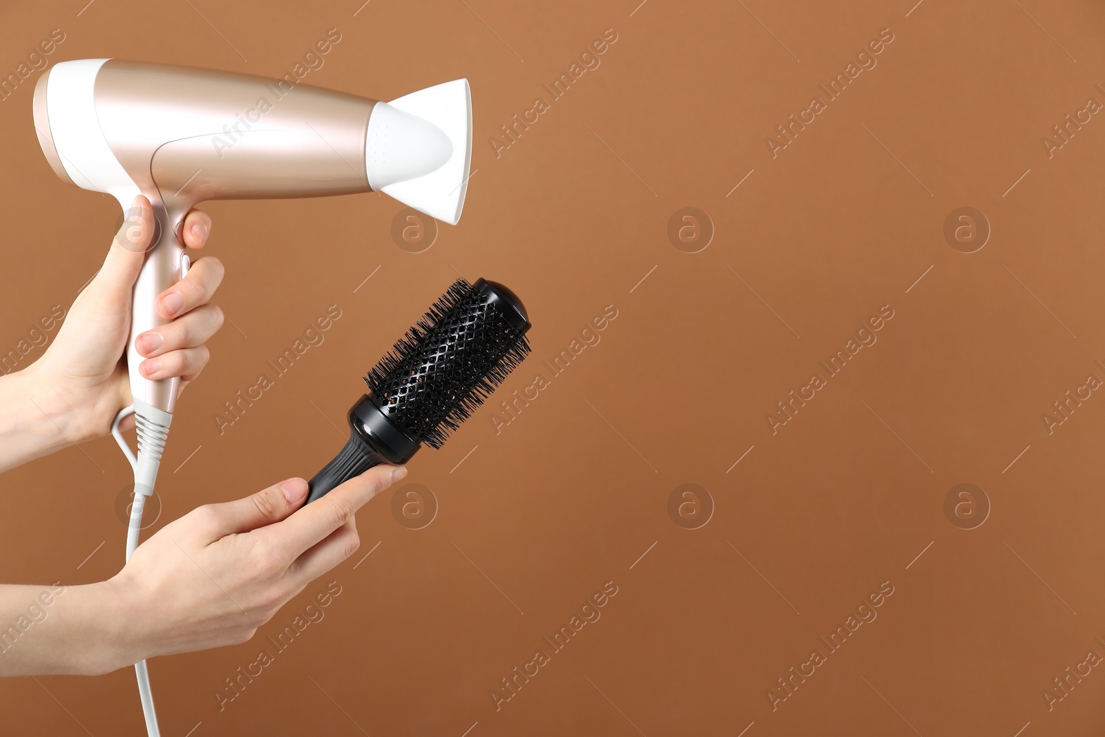 Photo of Woman with hair dryer and round brush on brown background, closeup. Space for text
