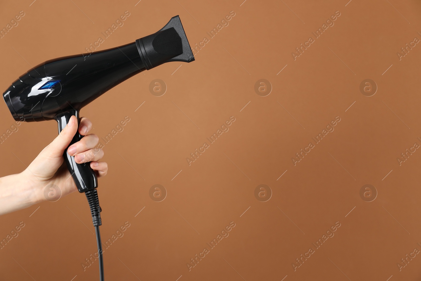 Photo of Woman with hair dryer on brown background, closeup. Space for text