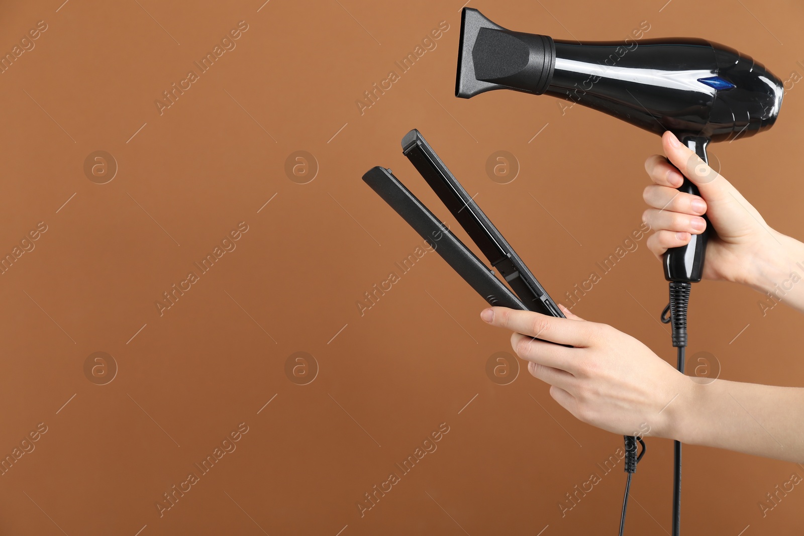 Photo of Woman with hair dryer and straightener on brown background, closeup. Space for text