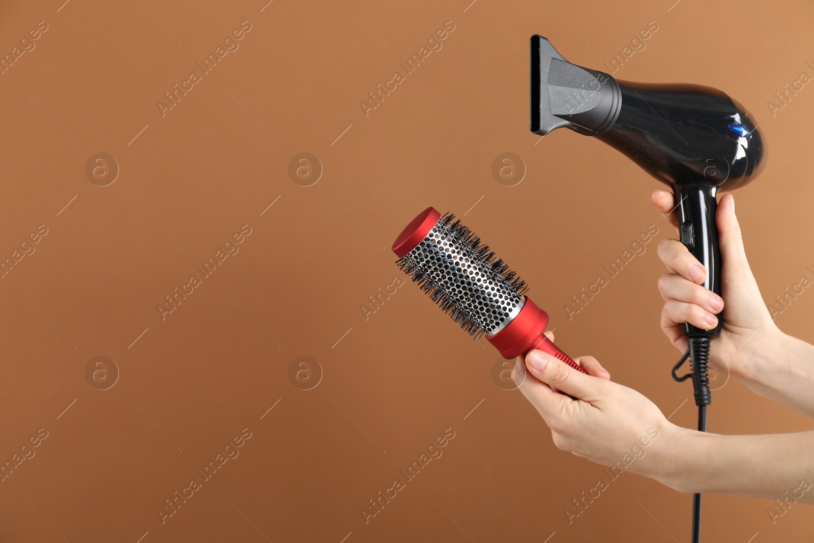 Photo of Woman with hair dryer and round brush on brown background, closeup. Space for text
