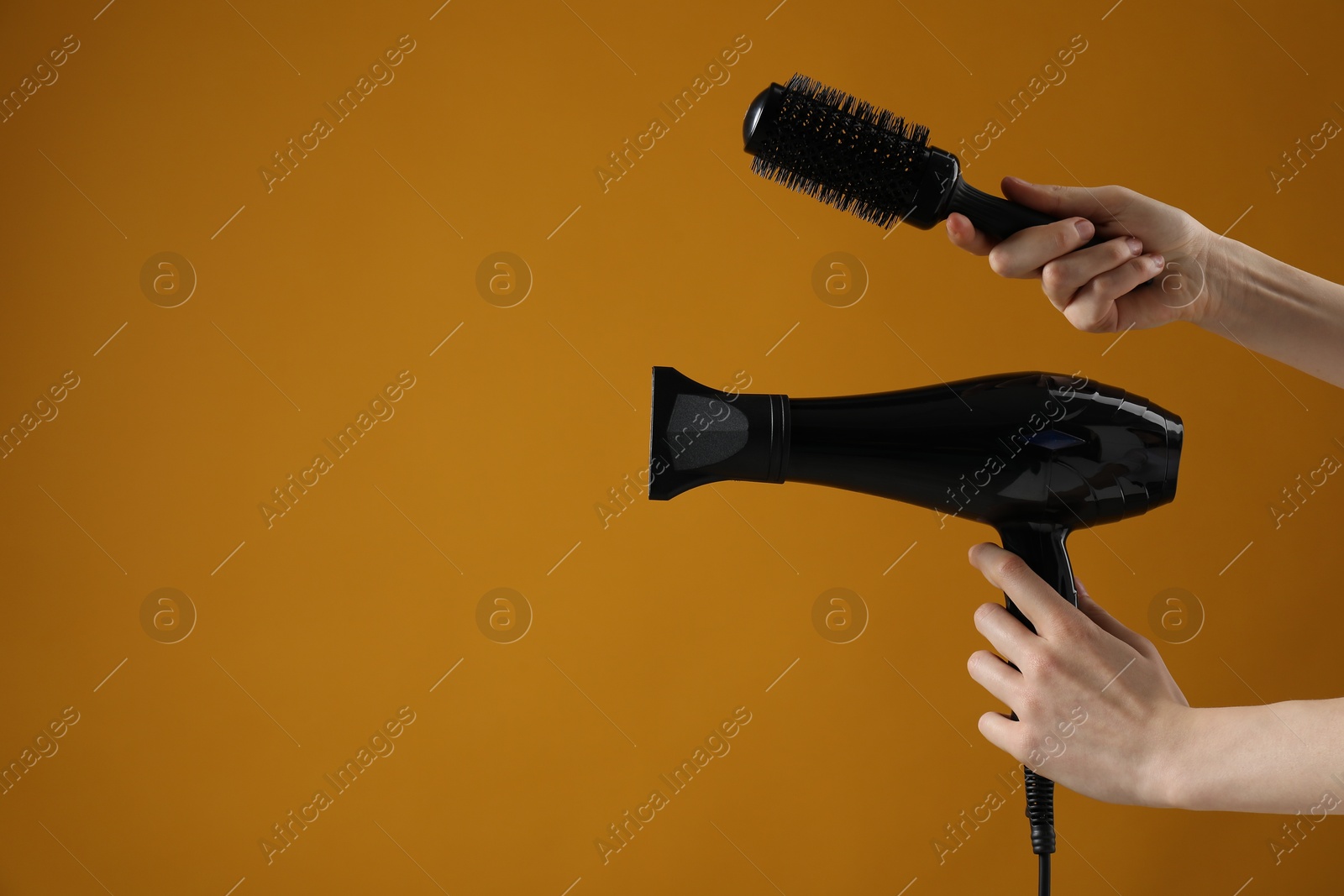 Woman with hair dryer and round brush on orange background, closeup. Space for text Photo of Woman with hair dryer and round brush on orange background, closeup. Space for text