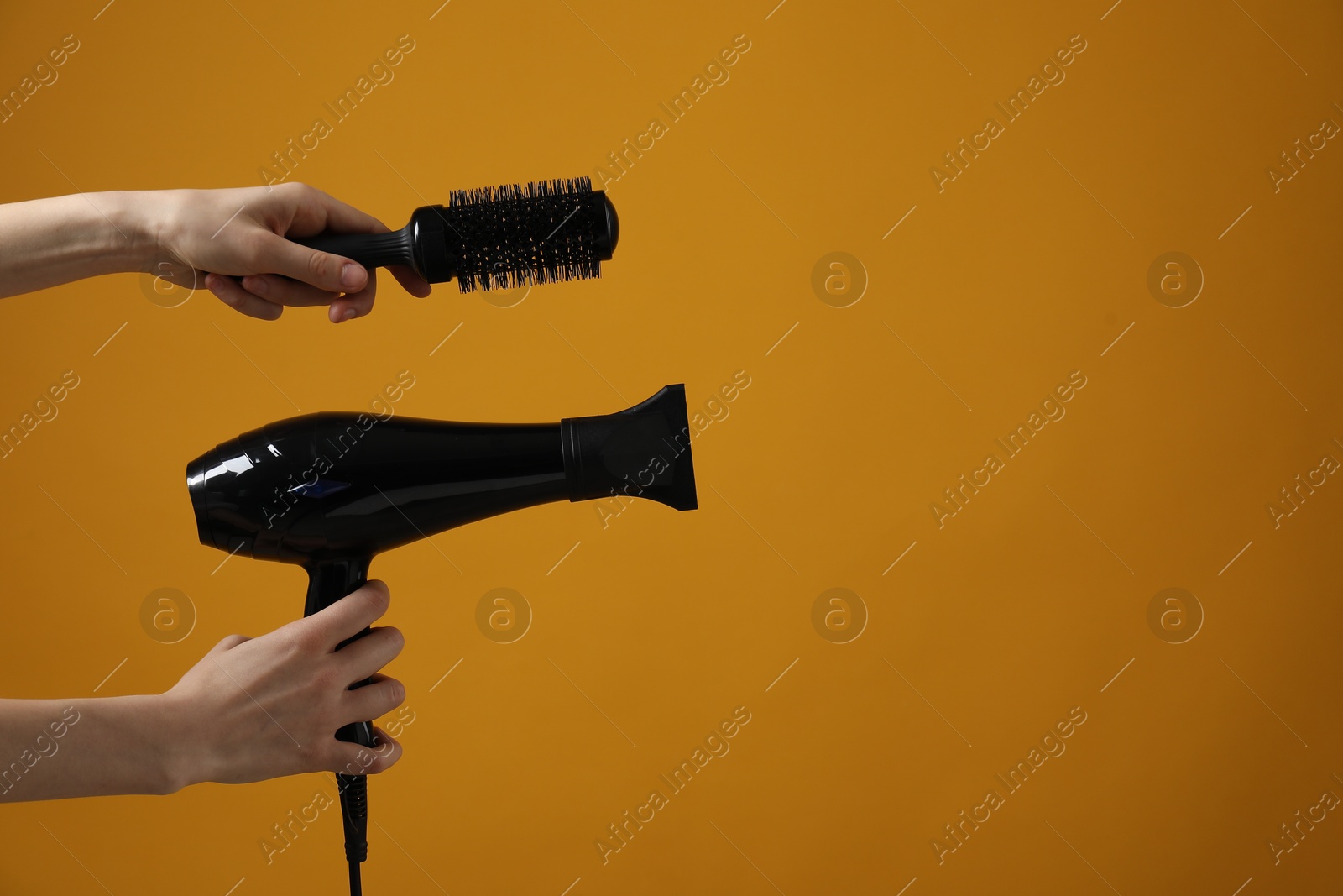 Photo of Woman with hair dryer and round brush on orange background, closeup. Space for text