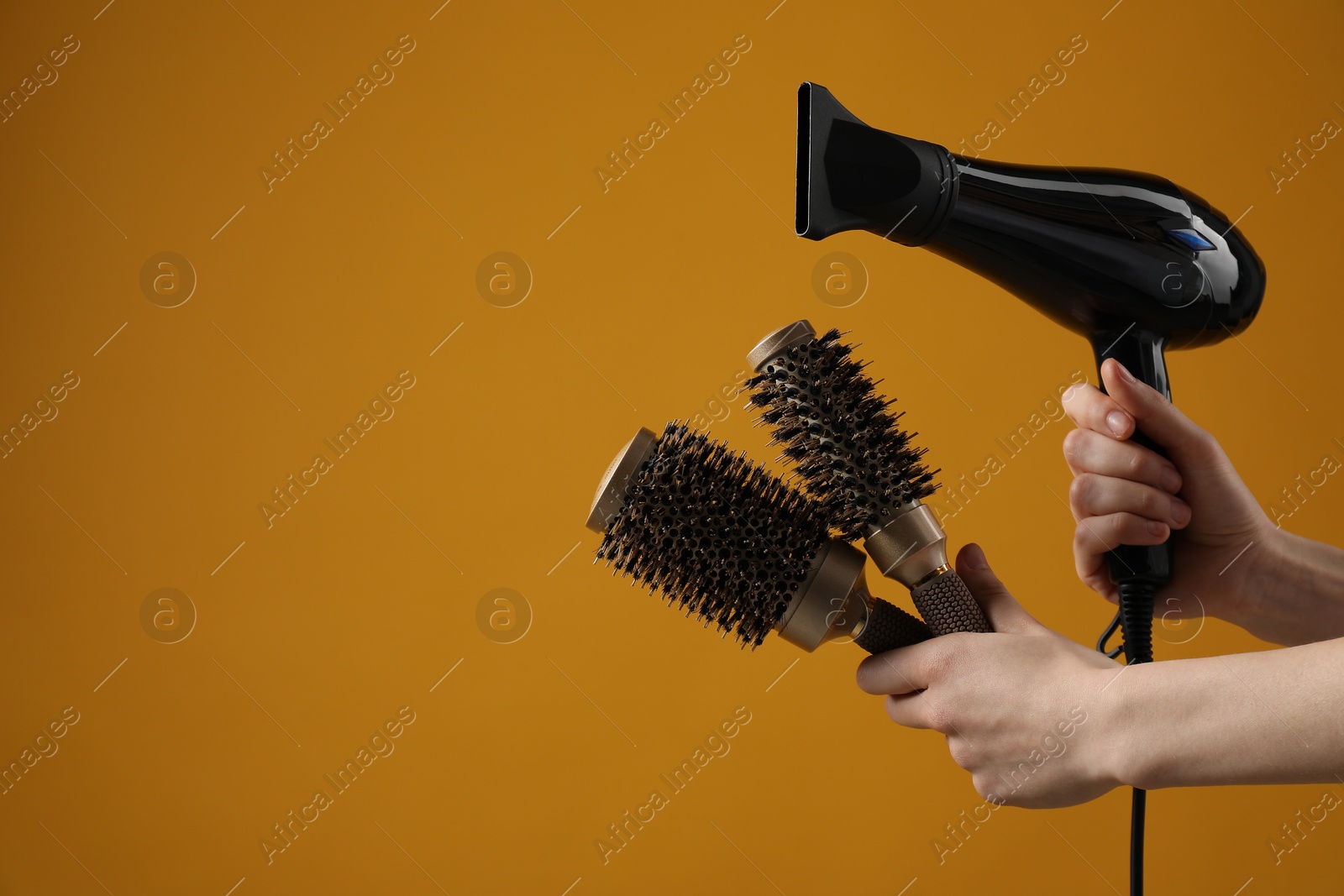 Woman with hair dryer and round brushes on orange background, closeup. Space for text Photo of Woman with hair dryer and round brushes on orange background, closeup. Space for text