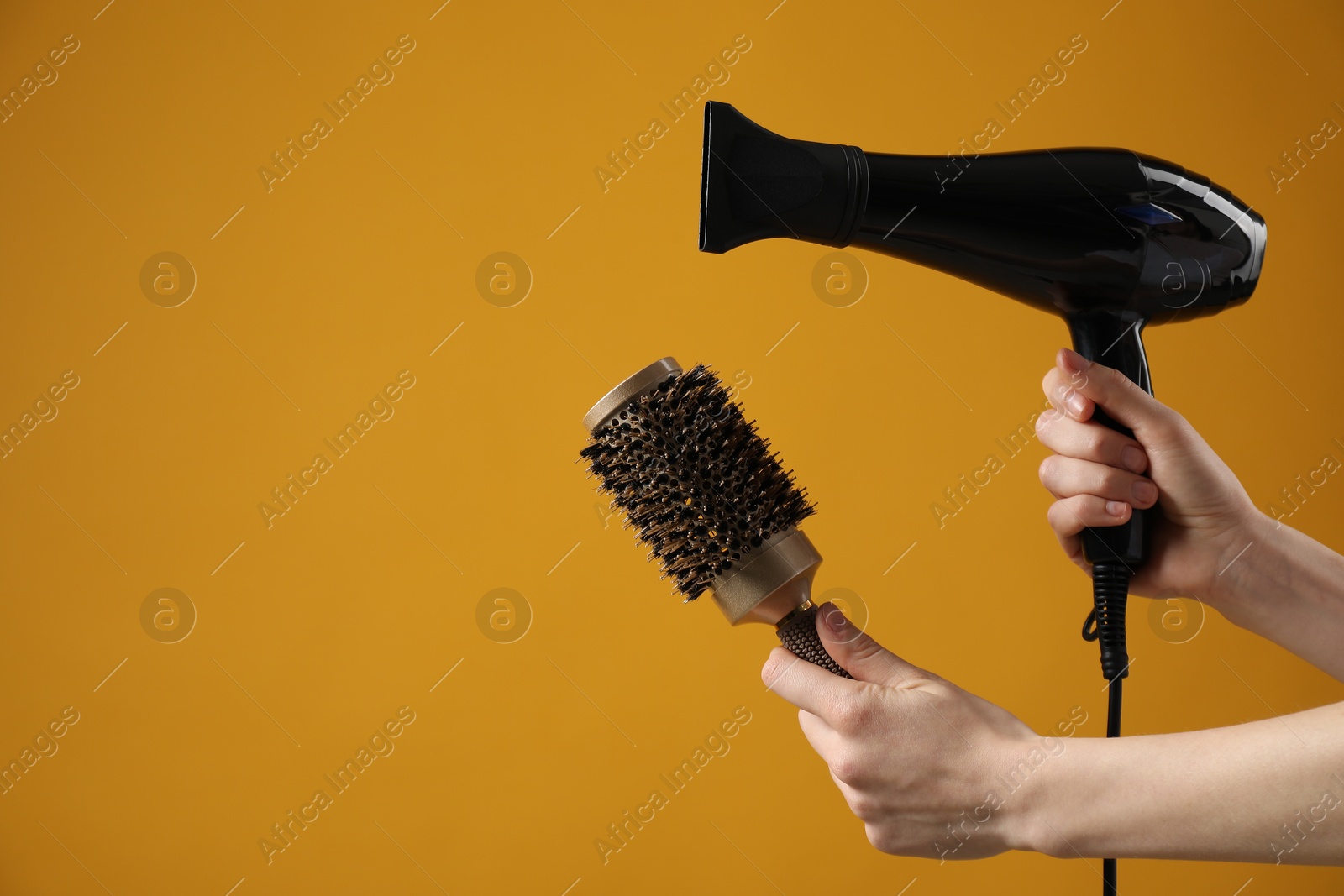 Photo of Woman with hair dryer and round brush on orange background, closeup. Space for text