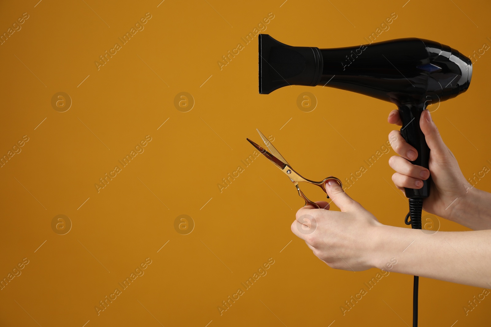 Woman with hair dryer and scissors on orange background, closeup. Space for text Photo of Woman with hair dryer and scissors on orange background, closeup. Space for text