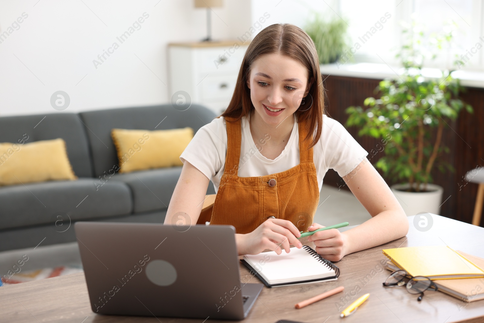 Teenage girl doing homework with laptop at table indoors Photo of Teenage girl doing homework with laptop at table indoors
