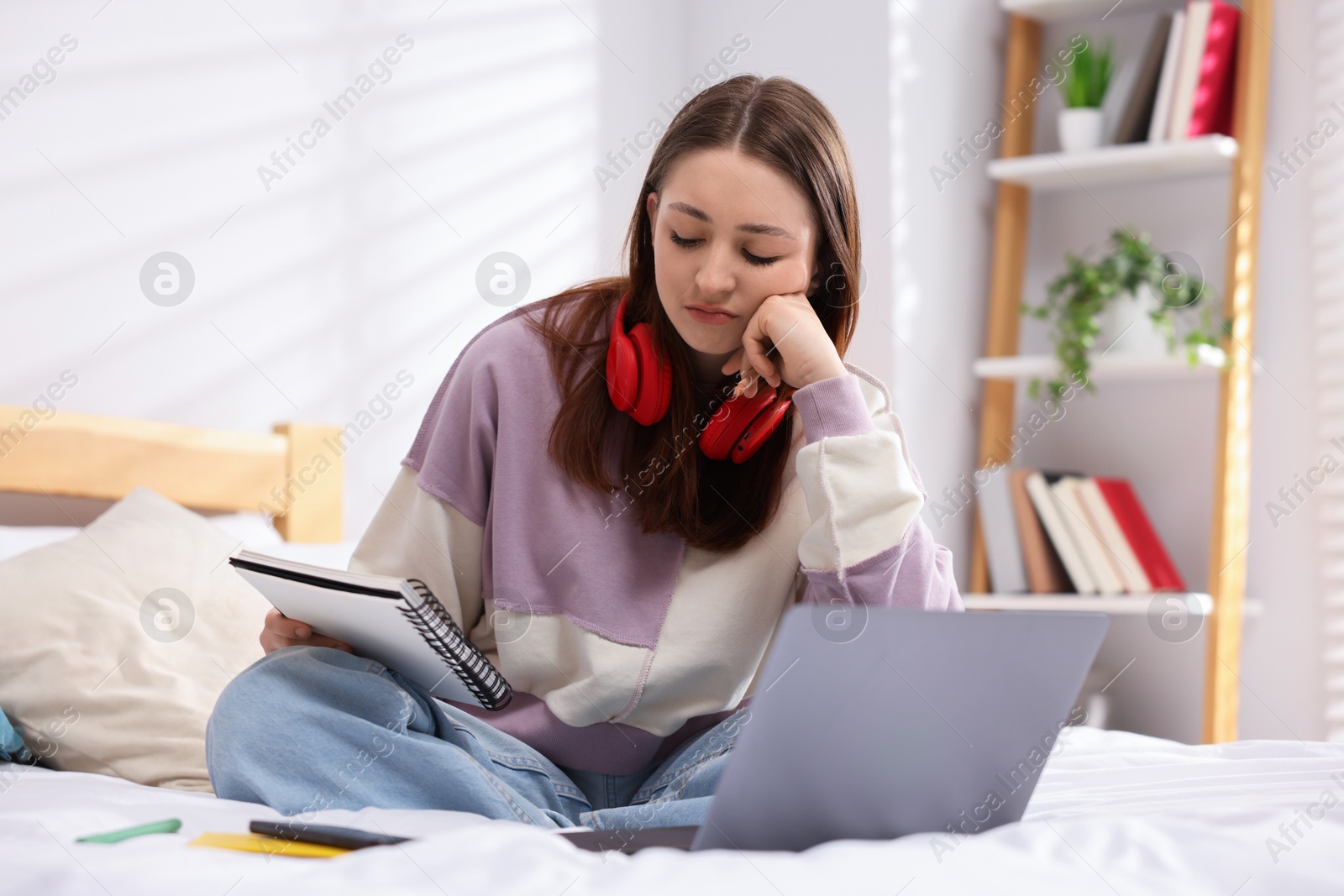 Photo of Teenage girl doing homework near laptop on bed at home
