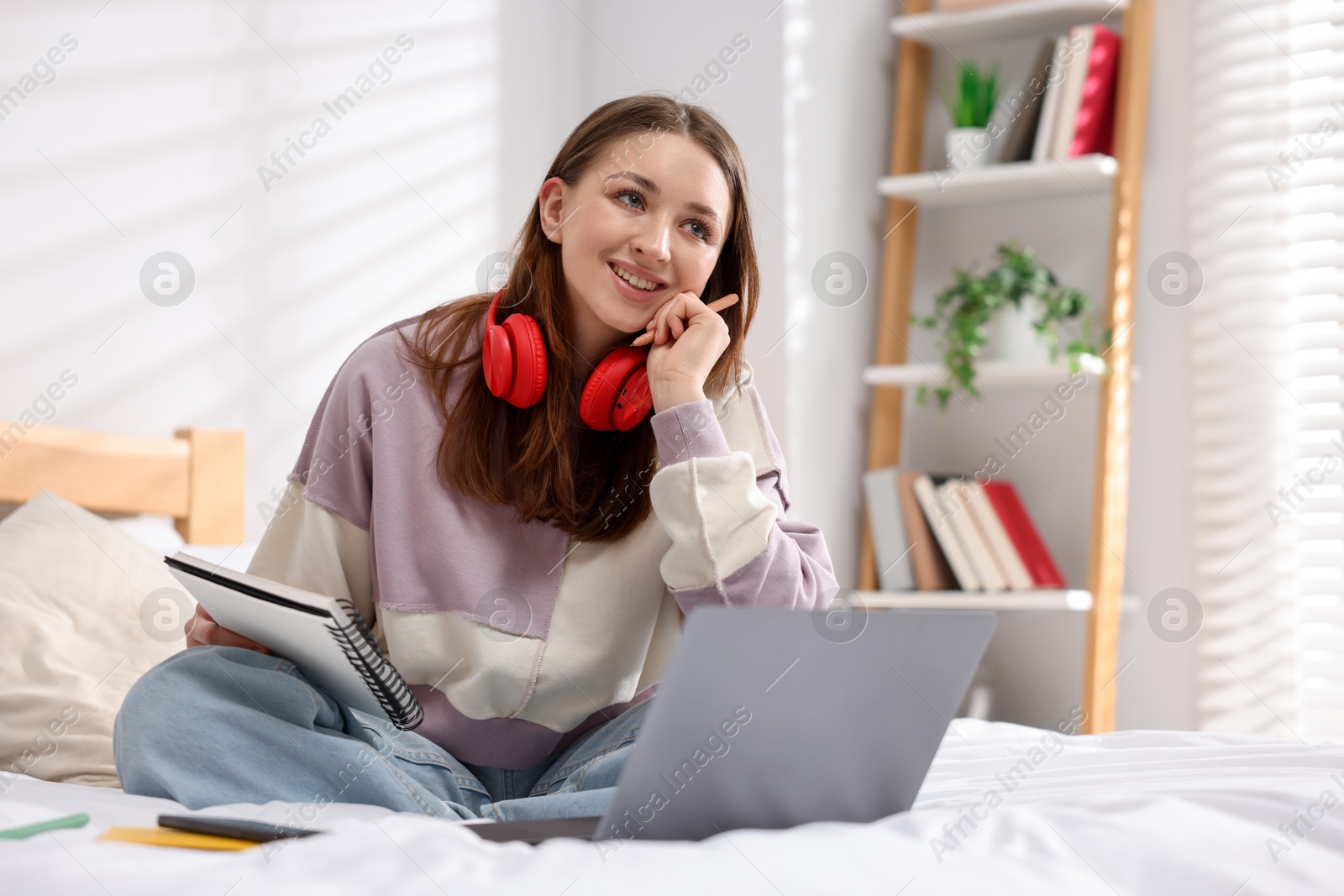 Teenage girl doing homework near laptop on bed at home Photo of Teenage girl doing homework near laptop on bed at home
