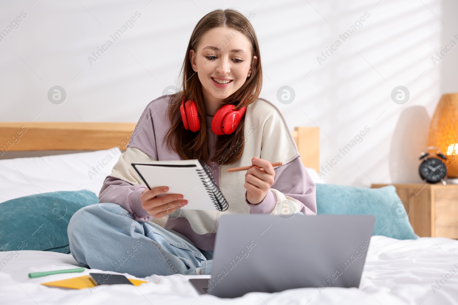 Photo of Teenage girl doing homework near laptop on bed at home