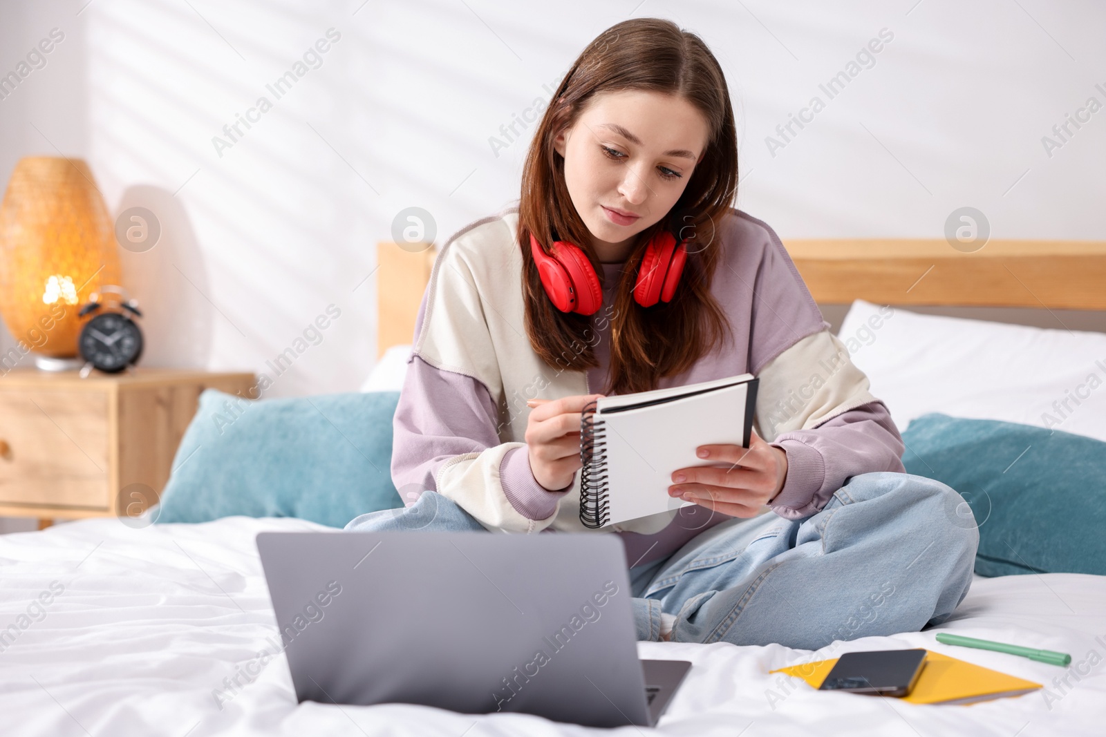 Teenage girl doing homework near laptop on bed at home Photo of Teenage girl doing homework near laptop on bed at home