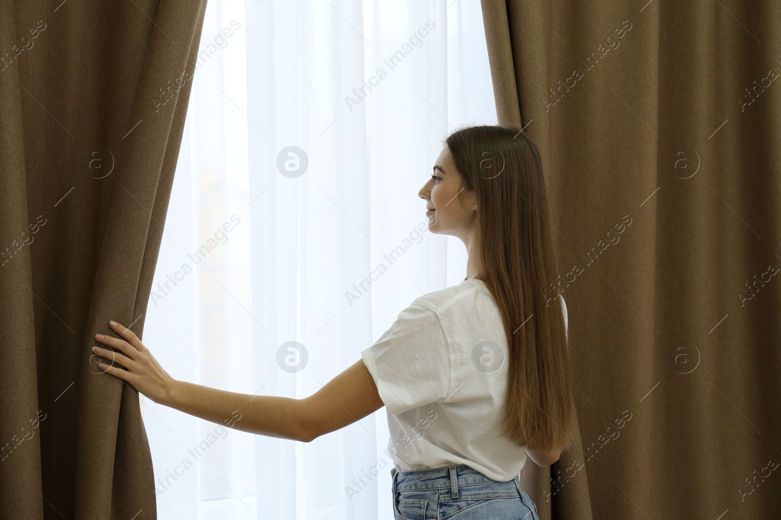 Woman opening elegant window curtains in room Photo of Woman opening elegant window curtains in room