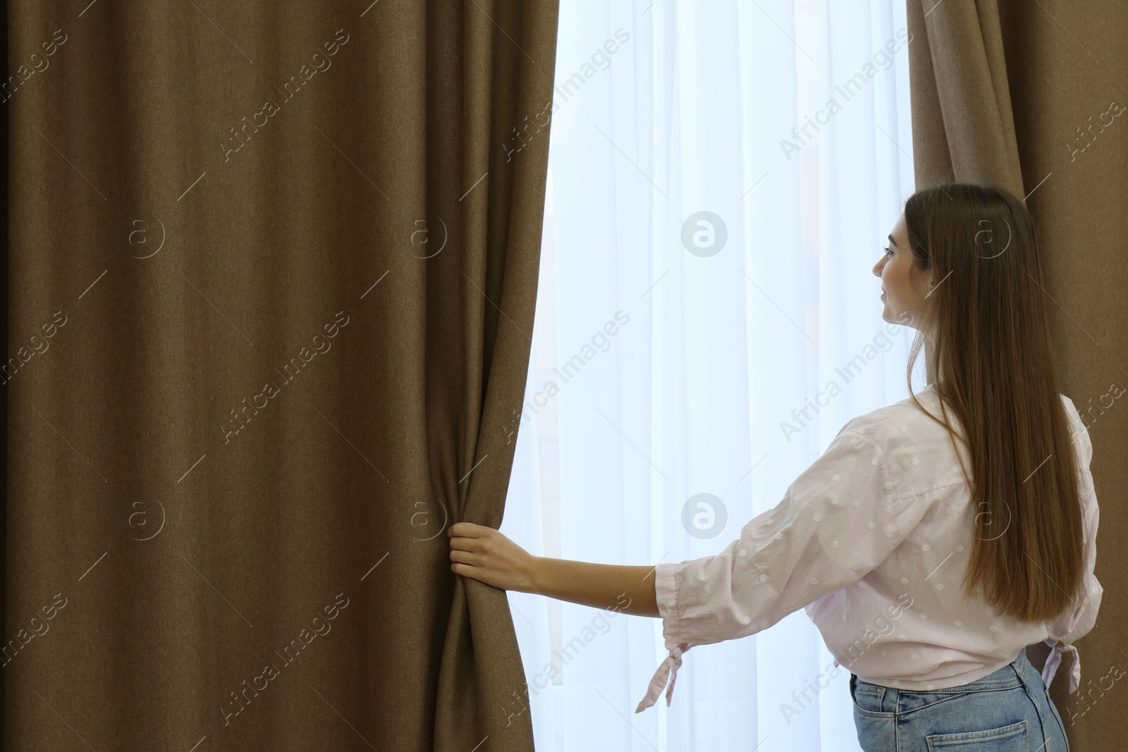 Woman opening elegant window curtains in room, back view Photo of Woman opening elegant window curtains in room, back view